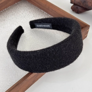 Detail view of a thick black wool headband featuring a handmade fabric tag on inner band