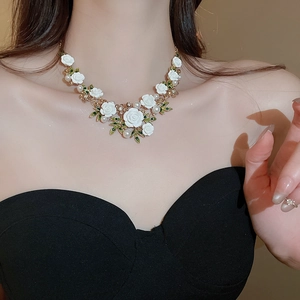 Detailed close-up of a floral pearl necklace with white roses and green leaves on a model
