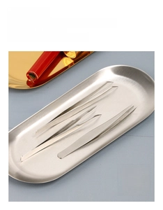 Close-up of a silver oval stainless steel jewelry tray with precision metal tweezers