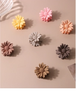 Detail of colorful daisy hair clips in various matte pastel colors on a beige surface