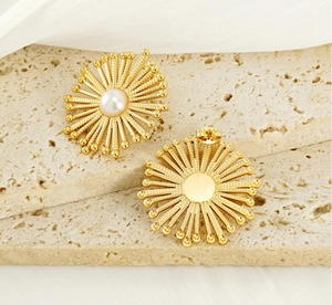 Detail view of golden bohemian flower stud earrings with central pearl on travertine stone