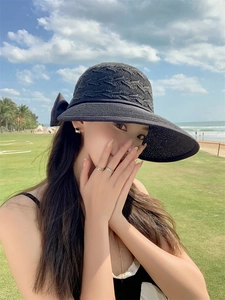 Detail of black woven straw hat featuring a decorative bow on a sunny beach background