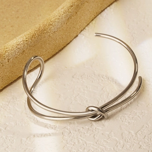Macro detail of the polished silver knot design on a minimalist open bangle bracelet