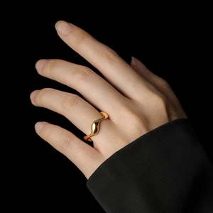 Macro detail of minimalist gold wavy ring with polished mirror finish on model's hand