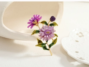 Detail of elegant purple enamel daisy brooch with gold trim and green leaves on a tray