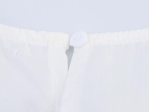 Détail de l'encolure en coton blanc avec un bouton rond et des coutures de broderie fines
