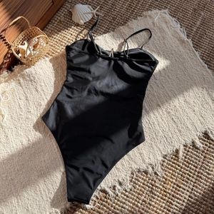 Detail of black one-piece swimsuit featuring chic back cut-outs and golden metal ring accents
