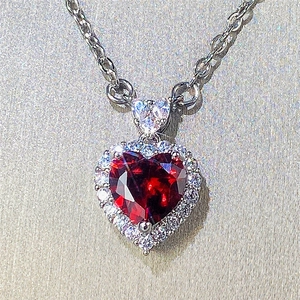 Detail of silver necklace featuring a red heart-shaped gemstone with diamond halo