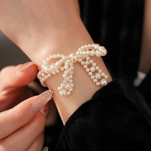 Detailaufnahme einer weißen Perlenarmband mit 3D-Schleifen-Design am Handgelenk