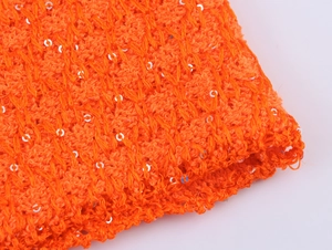 Makroaufnahme von orangefarbenem Strickstoff mit schimmernden silbernen Pailletten