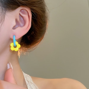 Detailed view of asymmetric blue hoop earring with yellow flower pendant on model