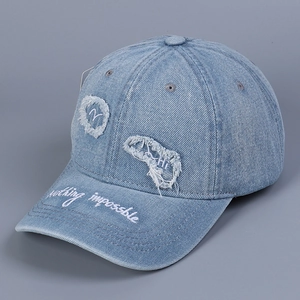 Dettaglio del cappellino in denim lavato con toppe sfrangiate e ricami in corsivo