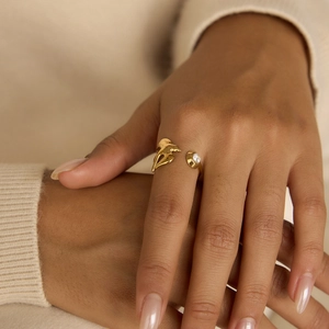 Close-up of golden olive leaf ring with a sparkling zircon on a model wearing a beige sweater