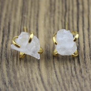Detail of natural raw white crystal stud earrings with gold claw settings on wood
