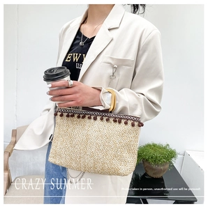 Detail of straw woven handbag featuring deep brown pom-poms and smooth wooden handles