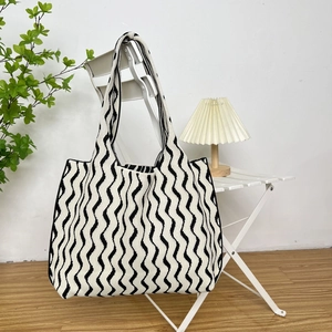 Close-up of black and white wave knit tote bag hanging on a white chair in a minimalist room