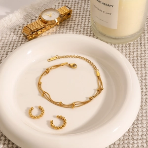 Gold-plated stainless steel multilayer bracelet and beaded jewelry set on white ceramic