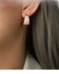 Close-up of model wearing gold-plated C-shaped crescent earrings with cream enamel finish