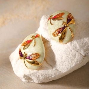 Close-up of gold-plated dragonfly earrings with green enamel on a natural stone base