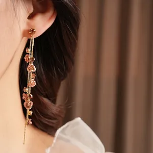 Elegant gold tassel earrings with rose flowers and crystals worn by a model
