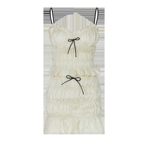 Close-up of beige pleated mini dress with black bows and ruffled hem details