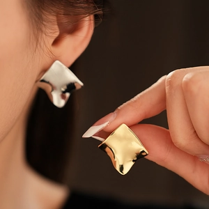 Détail de boucles d'oreilles carrées torsadées en finition or et argent sur un modèle