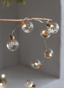 Close-up of LED warm light string with transparent snowflake glass balls on branches