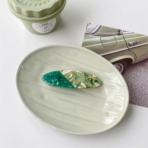 Detailed view of an oval tortoiseshell hair claw in green and yellow on a ceramic tray