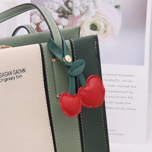 Close-up of red heart cherry keychain in PU leather on a green and beige handbag