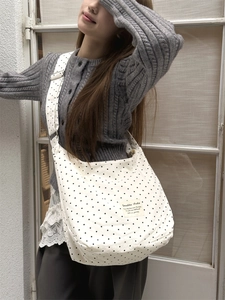 Detail shot of white polka dot canvas tote bag featuring a branded label and wide strap