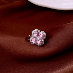 Macro shot of silver ring with pink zircon four-leaf clover petals on dark silk background