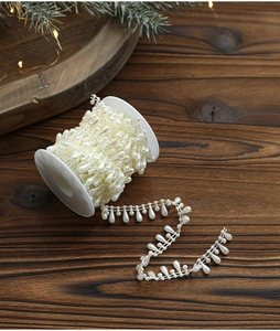 Close-up of cream white teardrop pearl ribbon roll on wooden table with holiday decor