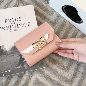 Close-up of pink litchi grain leather wallet with a golden bow metal buckle detail