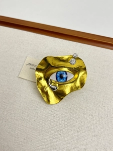 Macro shot of surrealist eye brooch featuring gold wavy base and blue eyeball detail