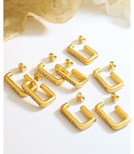 Gros plan de boucles d'oreilles créoles rectangulaires dorées avec zircons sur fond blanc