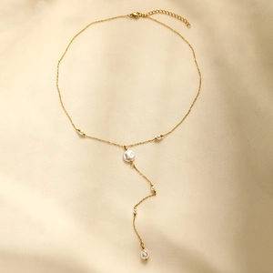 Macro detail of gold-plated Y-necklace featuring elegant white pearls on soft silk fabric