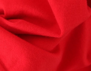 Macro view of soft red knitted fabric texture showing fine weave details and draping