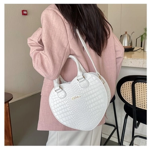 Sac à main blanc en forme de cœur motif crocodile porté à l'épaule dans un café