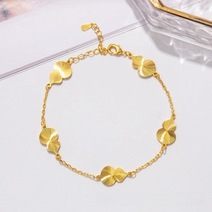 Detailed close-up of golden clover bracelet with radiating texture and lobster clasp