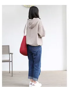 Rear view of a red canvas tote bag styled with an oversized hoodie and blue jeans