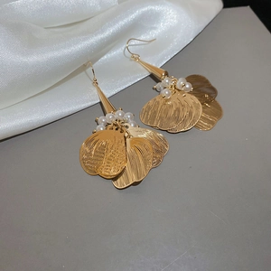 Close-up of golden petal earrings with pearl accents and brushed metal texture details
