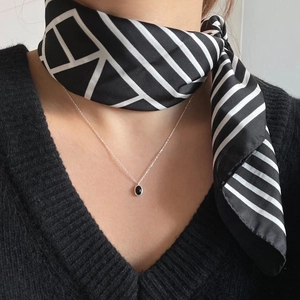 Detail of silver chain necklace with black oval pendant worn with a striped silk scarf
