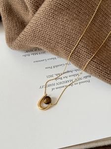 U-shaped stainless steel necklace with tiger eye bead on warm brown sweater background
