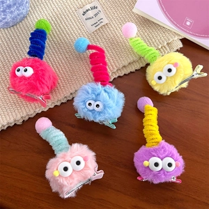 Set of five colorful plush monster hair clips with 3D eyes on beige woven mat