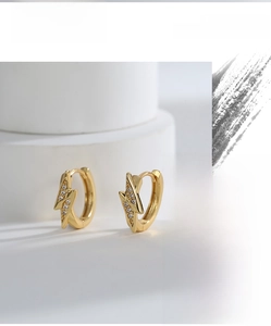 Close-up of golden lightning bolt earrings with white zircon on a white platform