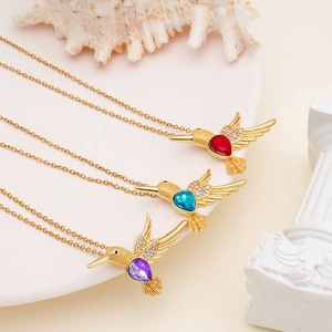 Three gold hummingbird necklaces with red, blue, and purple crystal pendants on white decor