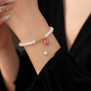 Detail of a pearl bracelet featuring a pink enamel dragon fruit charm and gold clasp