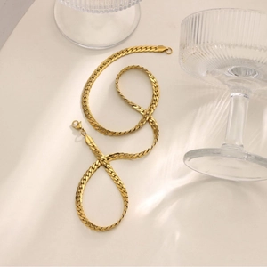 Flat gold-plated curb chain with lobster clasp on beige surface with glass shadow