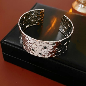 Macro detail of silver wide hollow cuff bracelet with hammer texture on black leather