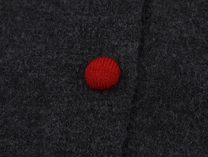 Detailed close-up of a red knitted button on contrast dark grey knit cardigan fabric